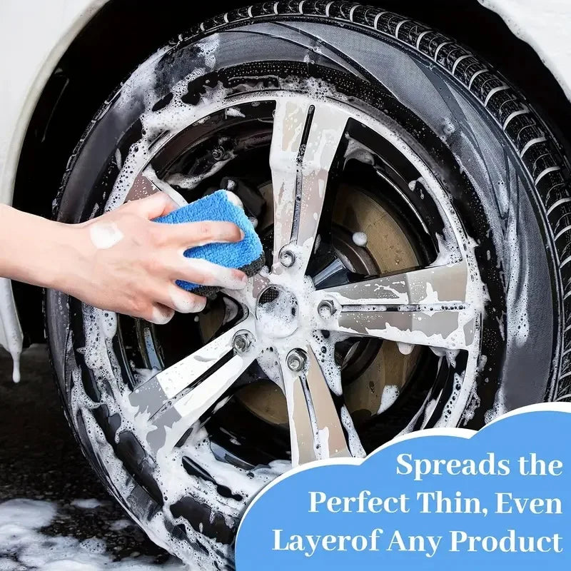 A hand applies a cleaning product to a black car wheel using a blue microfiber pad.
