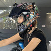 A person wearing a black t-shirt and a detailed, multi-colored motorcycle helmet is shown in an indoor setting.