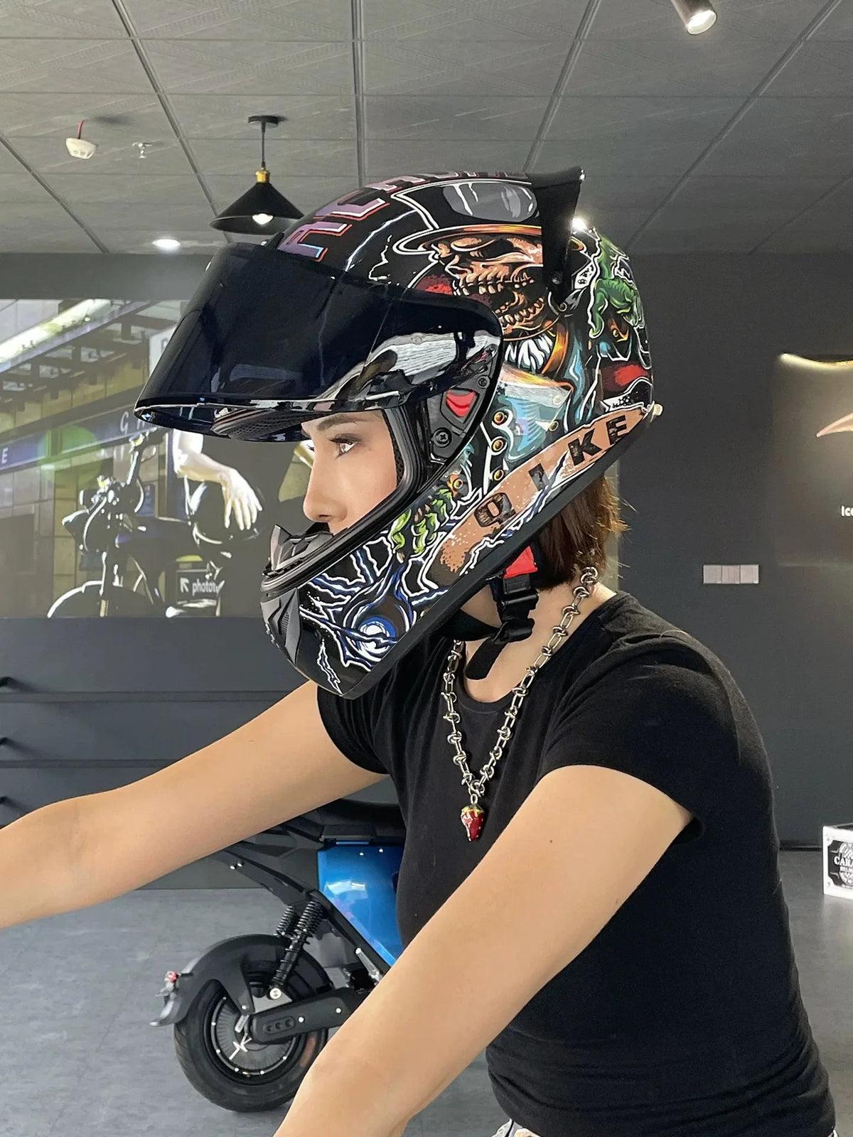 A person wearing a black t-shirt and a detailed, multi-colored motorcycle helmet is shown in an indoor setting.