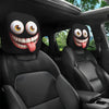 A pair of funny cartoon car headrest covers with big eyes and tongue-out designs installed in a black car interior.