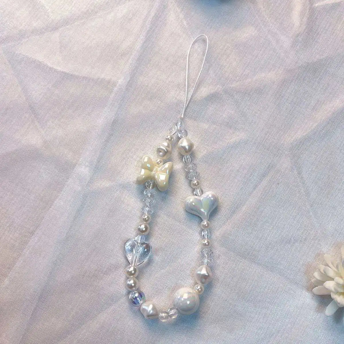 A delicate silver phone lanyard featuring a round bead pendant and a small bow charm.