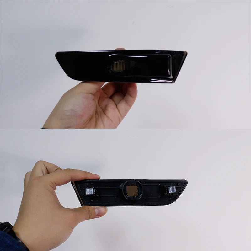 A hand holds a black smoked lens side marker light housing for an Infiniti G35.