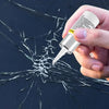 A hand holds a white kit for repairing automotive windshield cracks on a dark, shattered glass surface.