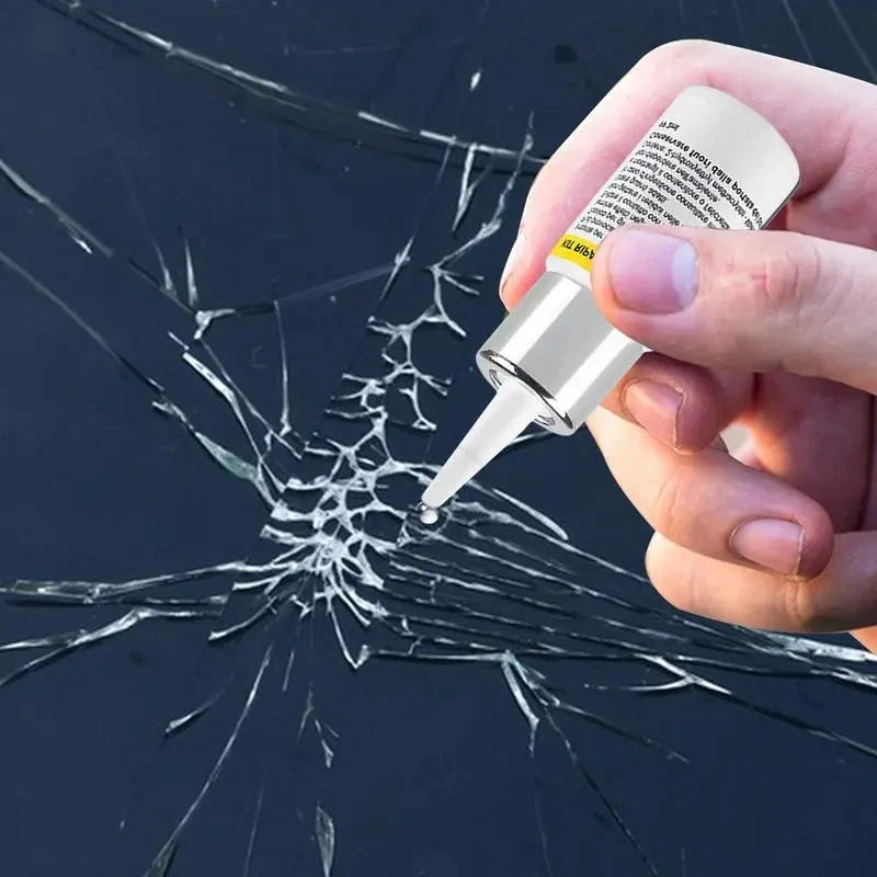 A hand holds a white kit for repairing automotive windshield cracks on a dark, shattered glass surface.