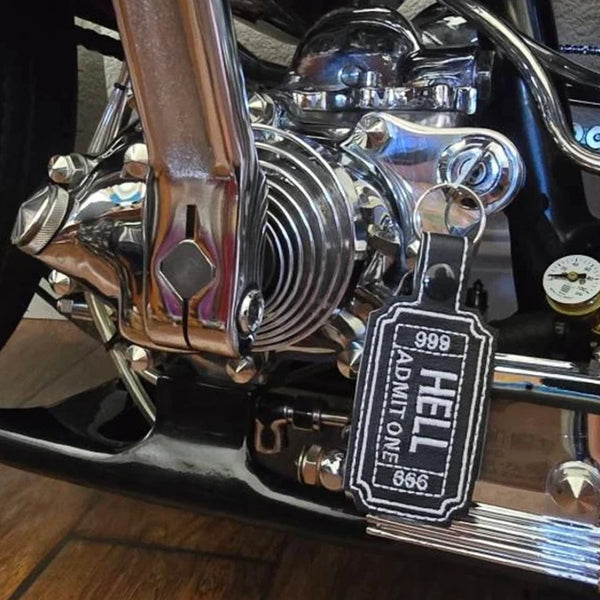 A close-up of a chrome motorcycle engine part and a black gothic keyfob luggage tag.