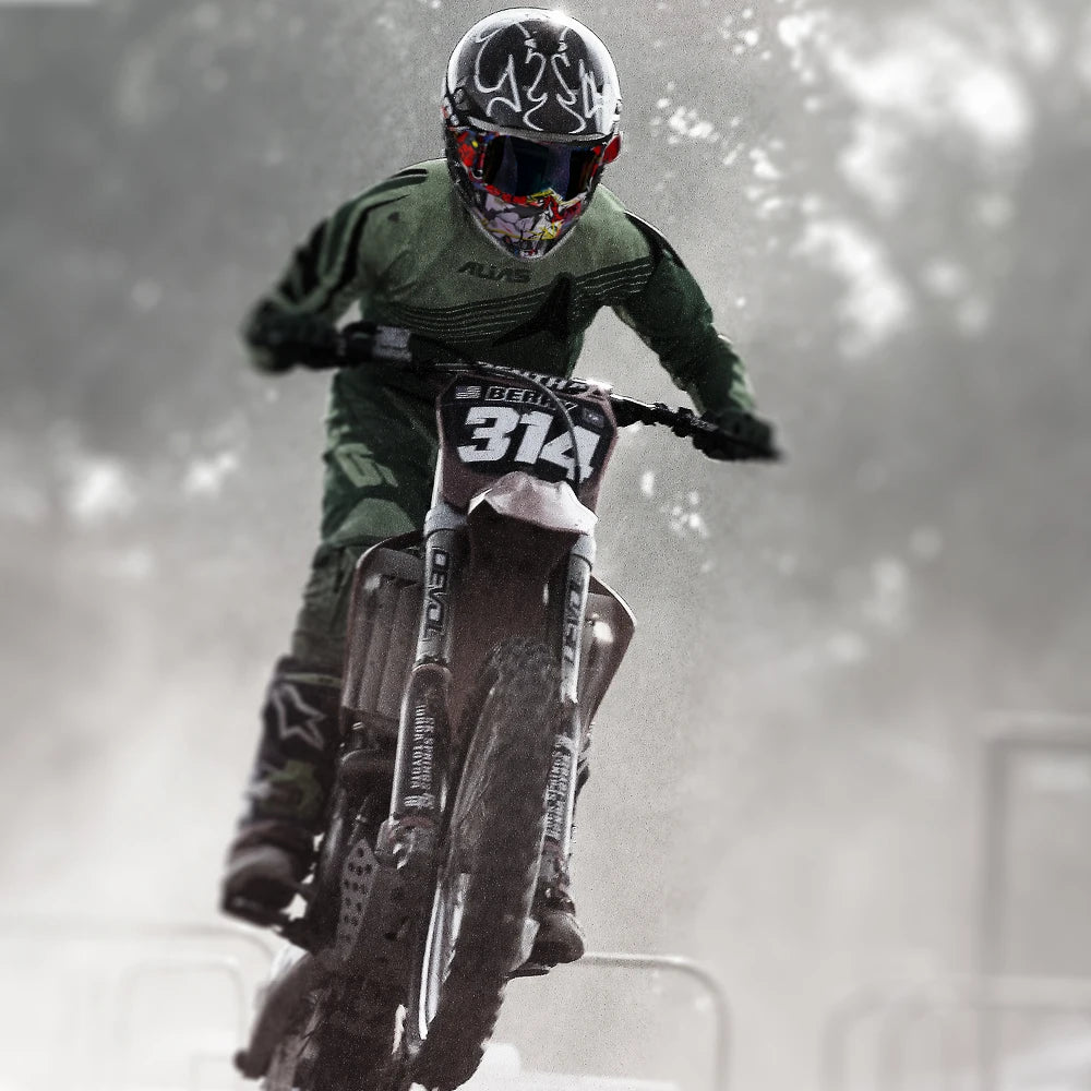 A rider wearing a full face helmet and goggles is performing a trick on a dirt bike in a foggy outdoor setting.