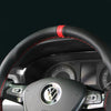 Close-up view of a black steering wheel with red stitching and a Volkswagen emblem.