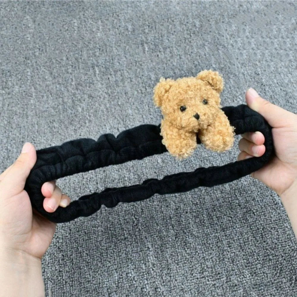 A hand holds a black plush toy resembling a teddy bear, which is a rearview mirror cover.