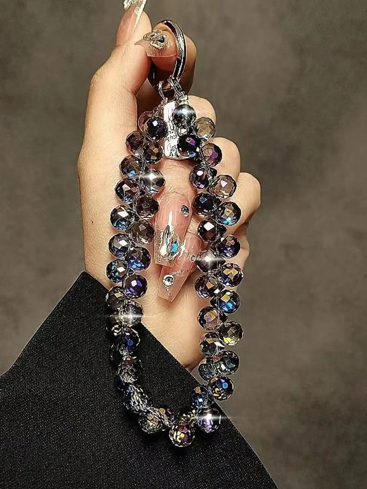 A hand holds a phone anti-loss lanyard featuring a strand of round, iridescent beads.