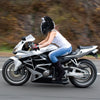 A woman wearing a white shirt and jeans rides a silver motorcycle with a black helmet on a road.