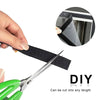 A hand is holding a black hook and loop tape strip, with a pair of scissors nearby, demonstrating the product for DIY project