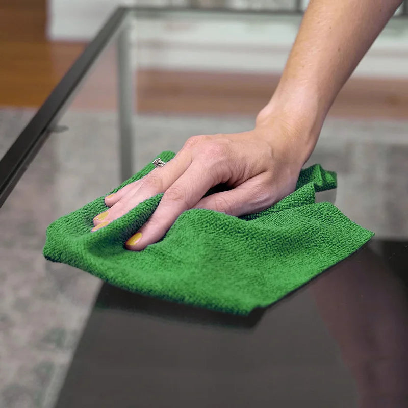A hand is holding a bright green reusable microfiber cleaning towel over a glass surface.