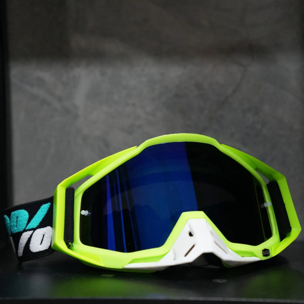 A pair of bright lime green and white high-performance motocross goggles resting on a dark surface.