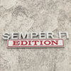 A silver metal badge with the text SEMPER FI EDITION on a red rectangular plaque.