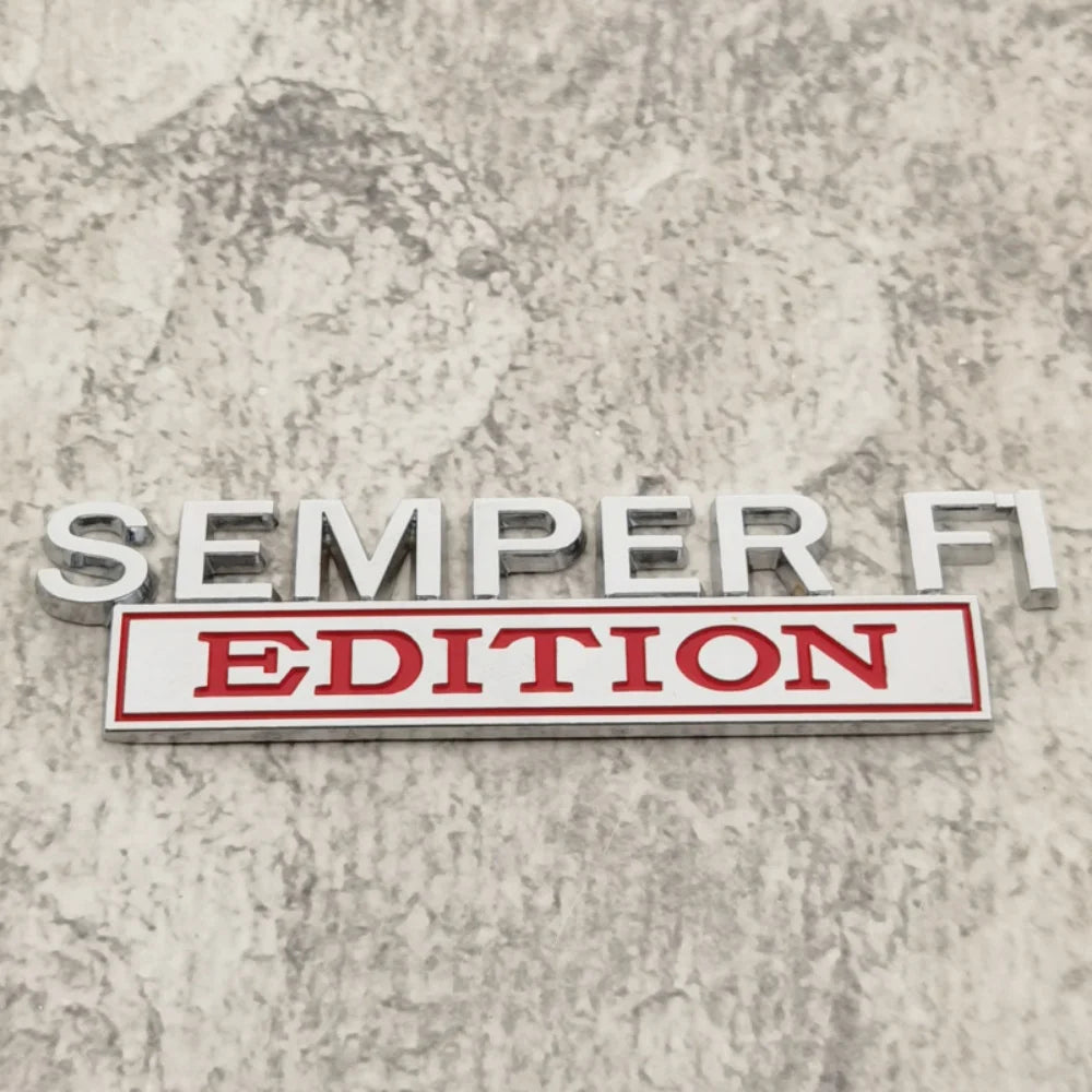 A silver metal badge with the text SEMPER FI EDITION on a red rectangular plaque.