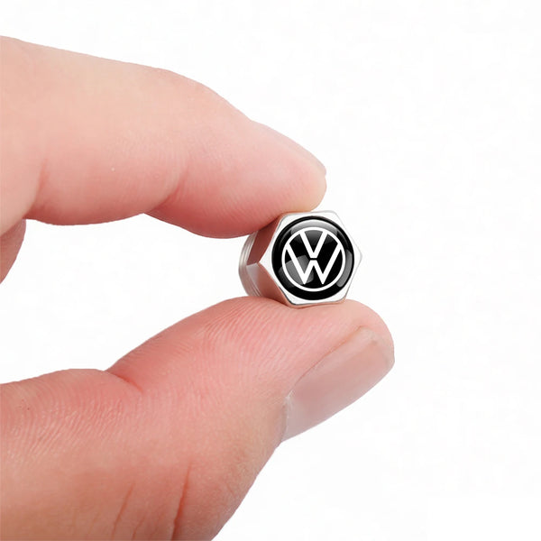A hand holds a silver Volkswagen tire valve cap with a black VW logo.