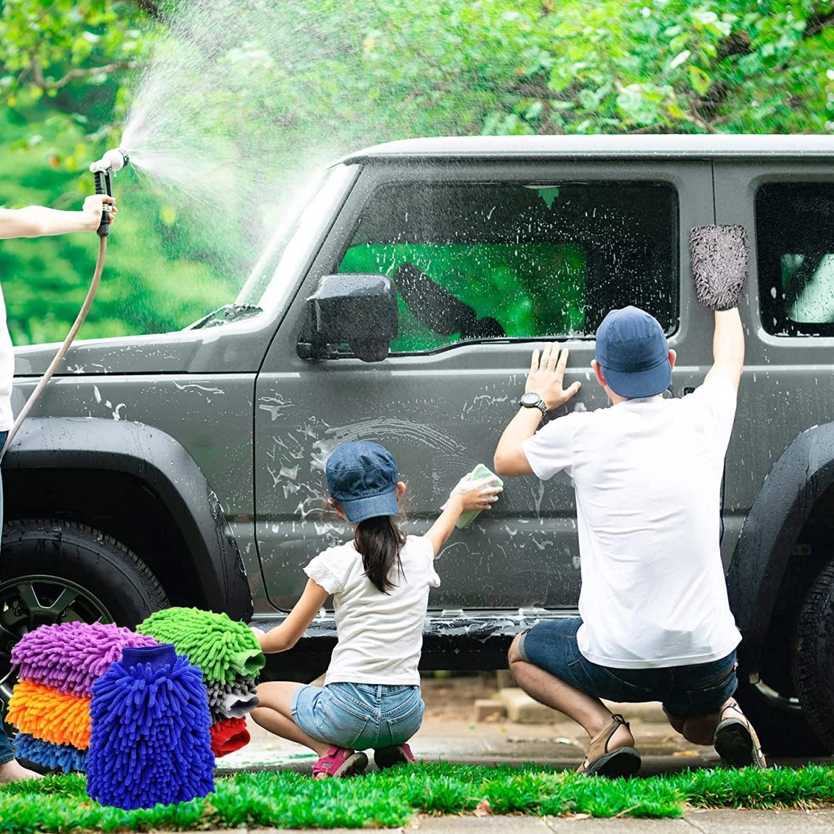 A person is washing a dark SUV with a water spray while another person uses a double-sided microfiber car wash mitt.