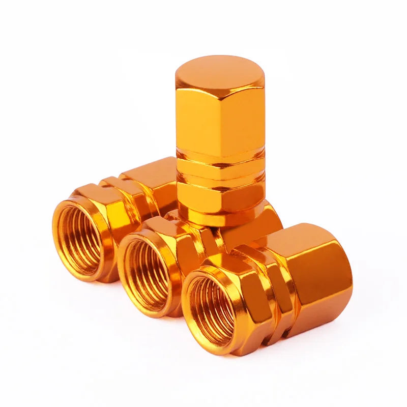 A set of four shiny gold-colored hex aluminum alloy tire valve caps stacked and laid out.