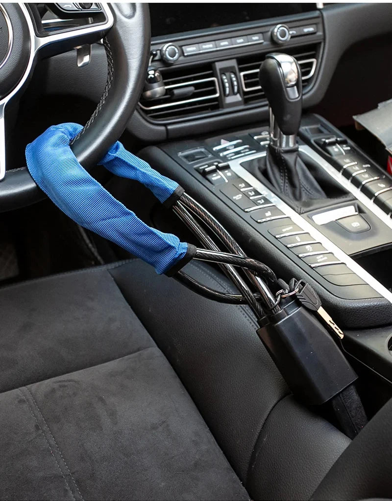 A blue strap attached to a steering wheel is connected via a cable to a seatbelt anti-theft lock device.