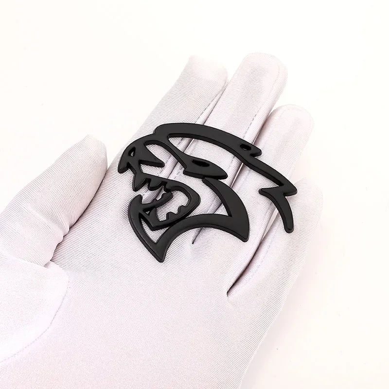 A black custom car body side emblem shaped like a snarling wolf head is displayed on a white glove.