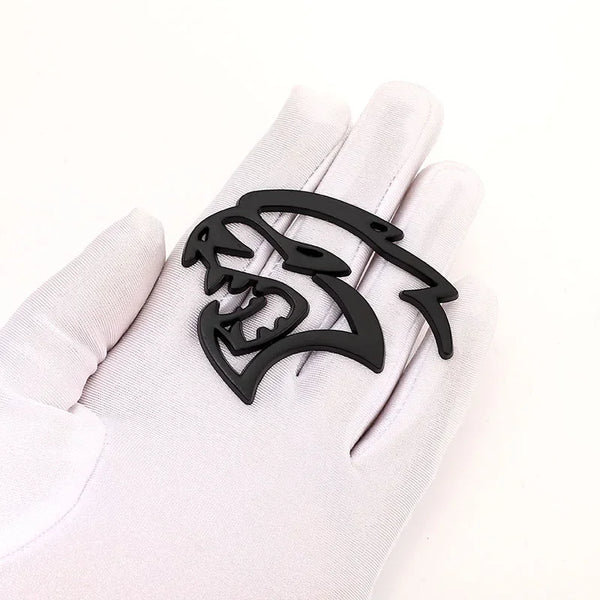 A black custom car body side emblem shaped like a snarling wolf head is displayed on a white glove.