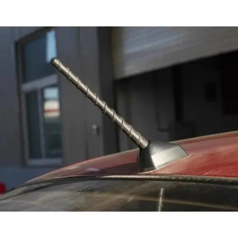 Close-up of a vehicle antenna with a threaded metal rod mounted on a red car roof.