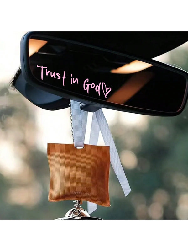 A black mirror with a pink heart inscription Trust in God on the glass, suspended by a white ribbon.