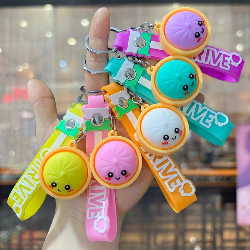 A hand holds several colorful silicone keychains featuring cute bao bun characters and various pastel colors.