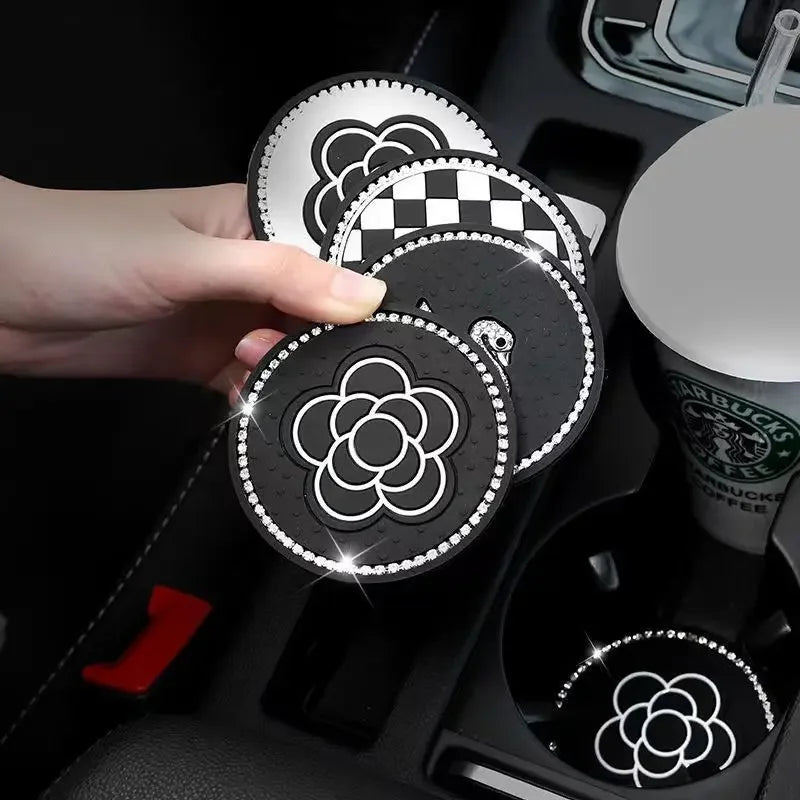A hand holds a set of two black silicone car cup coasters featuring a white floral design.