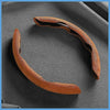 A brown suede steering wheel cover is shown curved on a dark surface.