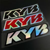 Three racing suspension decals featuring the KYB logo in black, red, and silver on a dark background.
