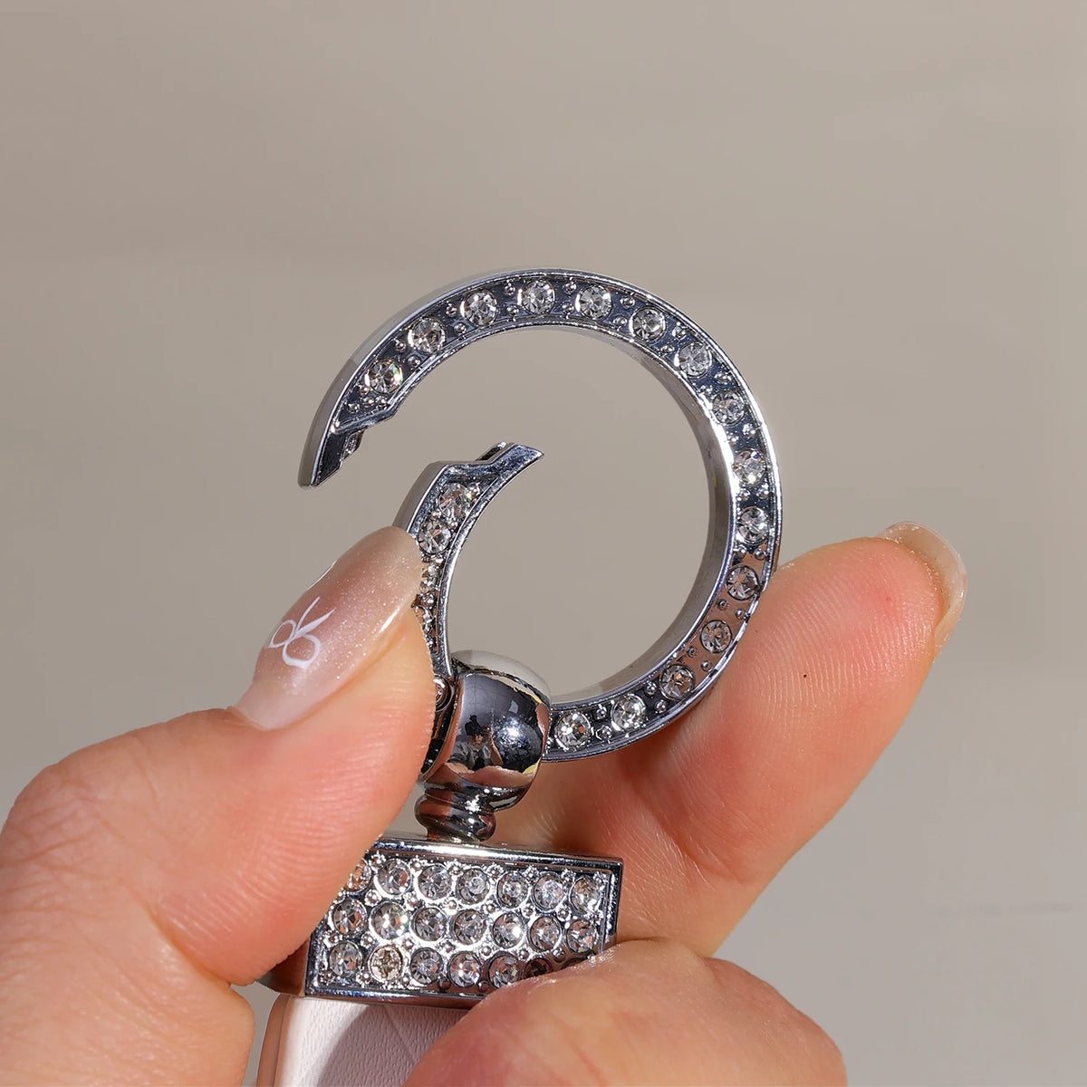 Eine Hand hält eine silberne Schleifen-Anhänger-Schlüsselanhänger mit Ring und rechtecklichem Anhänger vor hellem Hintergrund