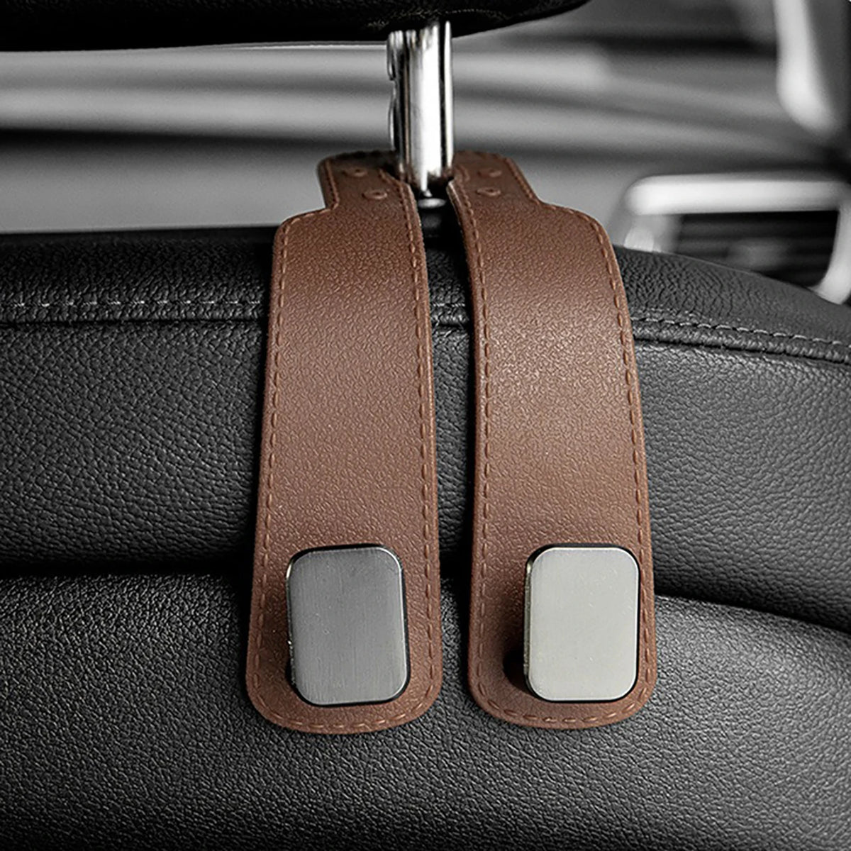 Two brown leather headrest hooks with silver accents are shown attached to a car seat.