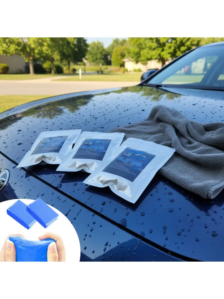 Several white clay bars are placed on a dark car hood next to a gray cloth and a blue cleaning block.