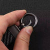 A hand holds a black and silver keychain with a carbon fiber texture and a metal ring.