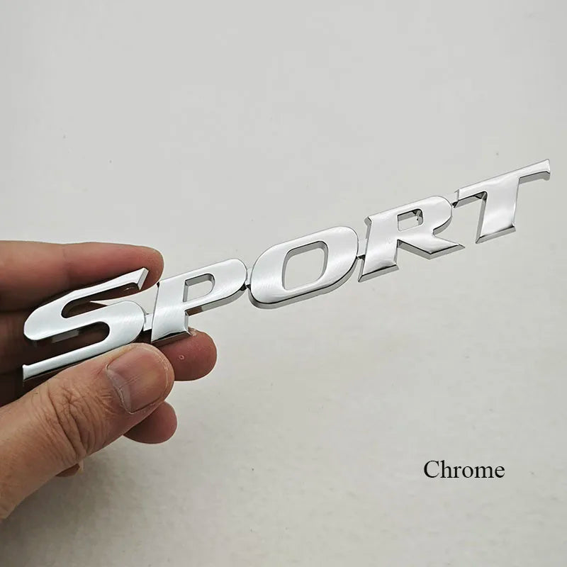 A hand holds a silver chrome SPORT text logo emblem for a car's rear trunk.