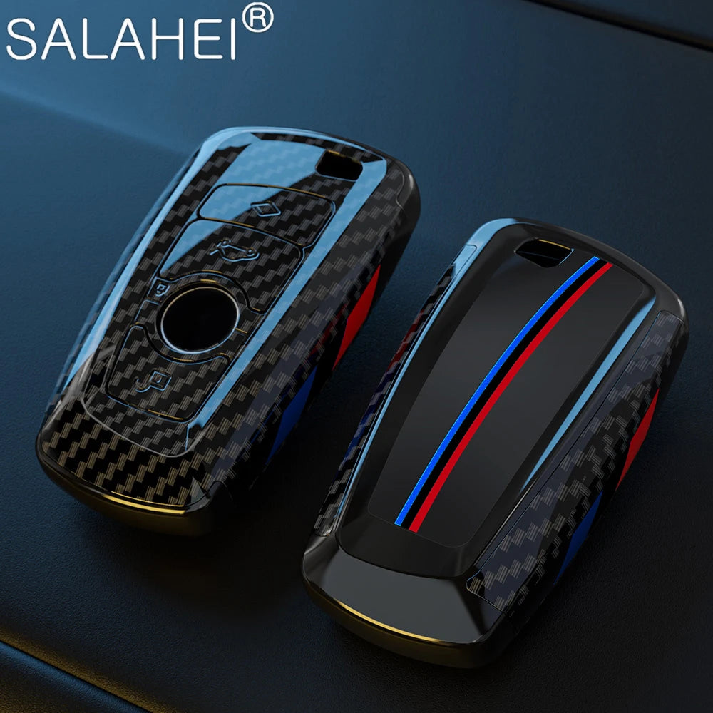 Un par de fundas para llaves de coche de fibra de carbono negra con detalles metálicos, sobre una superficie oscura.