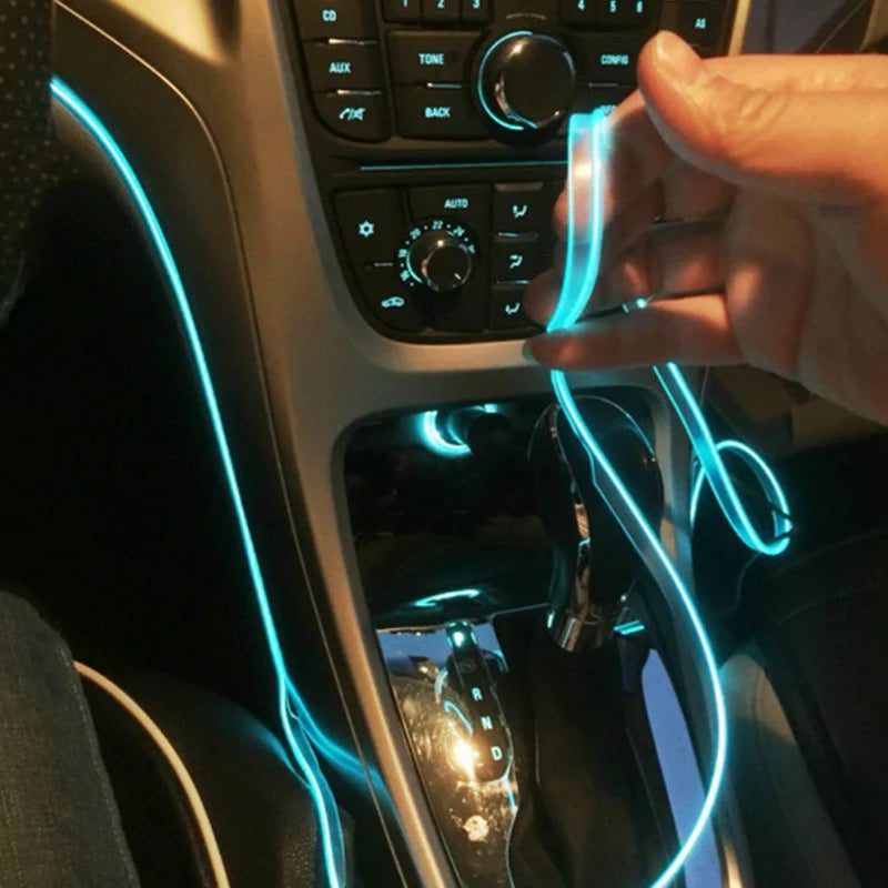 A hand is connecting a flexible blue LED strip to the interior of a car, illuminating the dashboard area.