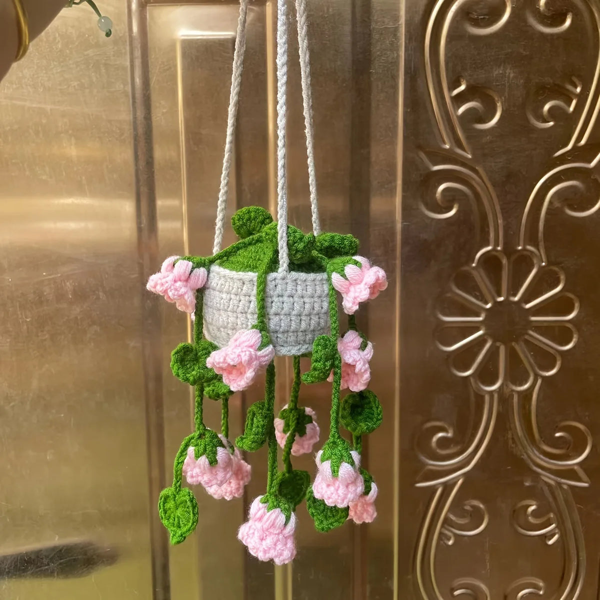 A hanging strawberry crochet decor featuring pink and green flowers suspended by twine.