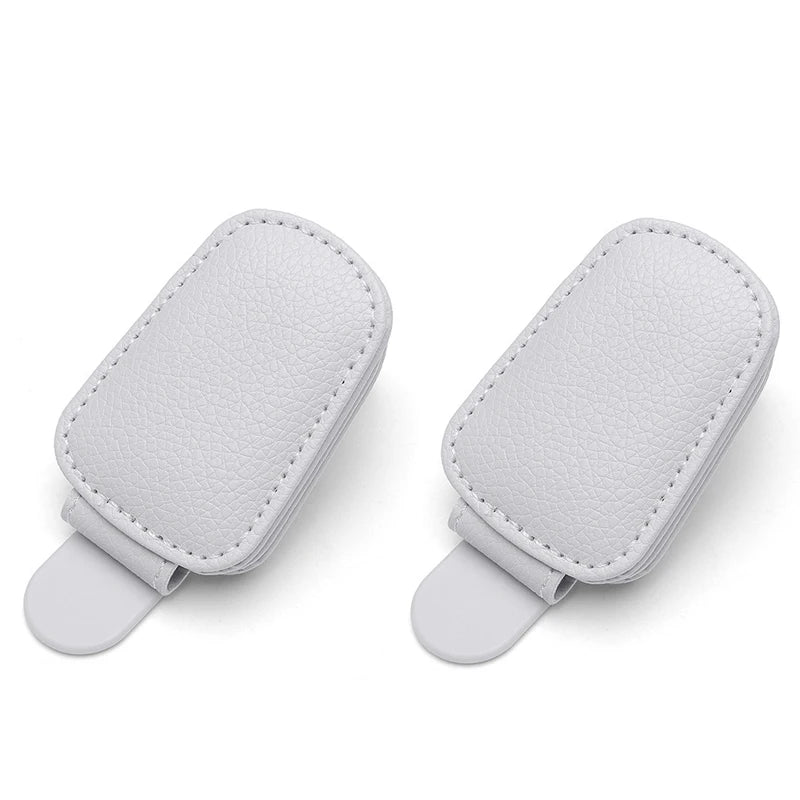 A pair of white magnetic leather sunglasses holders designed for car sun visors.