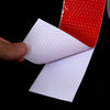 Una mano sostiene un material blanco reflectante junto a una tira de cinta de advertencia de PVC roja reflectante.