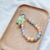A necklace featuring round beads in pastel shades of green, yellow, pink, and blue, displayed on a wooden tray.