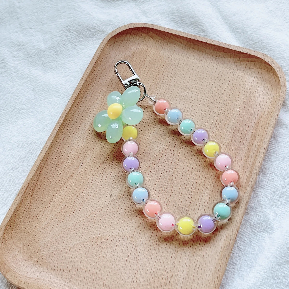 A necklace featuring round beads in pastel shades of green, yellow, pink, and blue, displayed on a wooden tray.