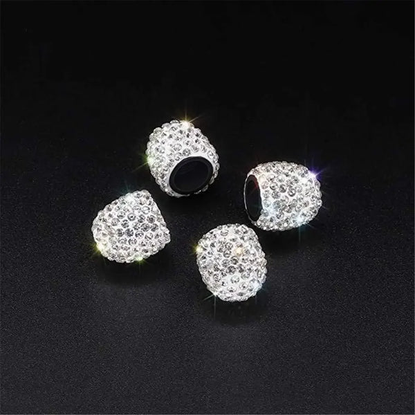 Three silver diamond-encrusted wheel valve caps are displayed on a dark surface.