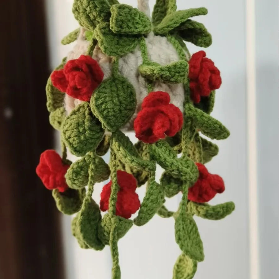 A hanging crochet decor featuring green leaves and red strawberry-like flowers.