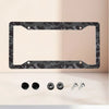 A black camouflage aluminum license plate frame with mounting holes and four silver bolts displayed on a light surface.