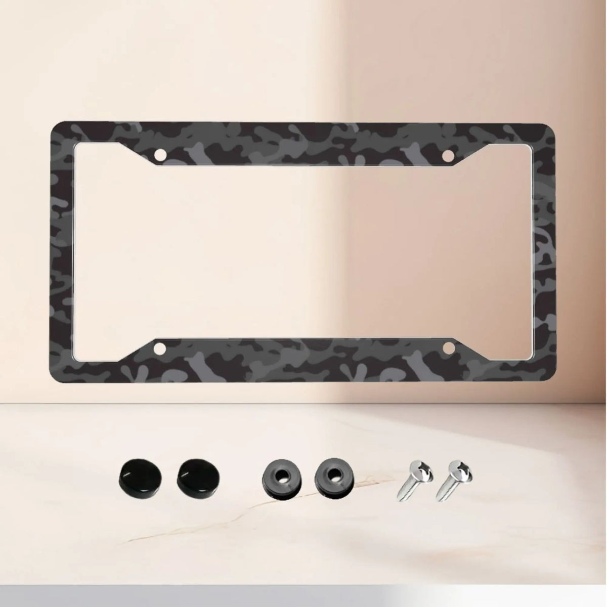 A black camouflage aluminum license plate frame with mounting holes and four silver bolts displayed on a light surface.