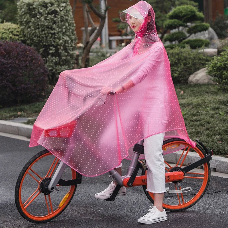 A woman wearing a sheer pink windproof poncho is riding an orange bicycle outdoors.