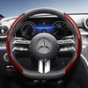Close-up view of a black steering wheel with red carbon fiber texture accents and a Mercedes-Benz logo.