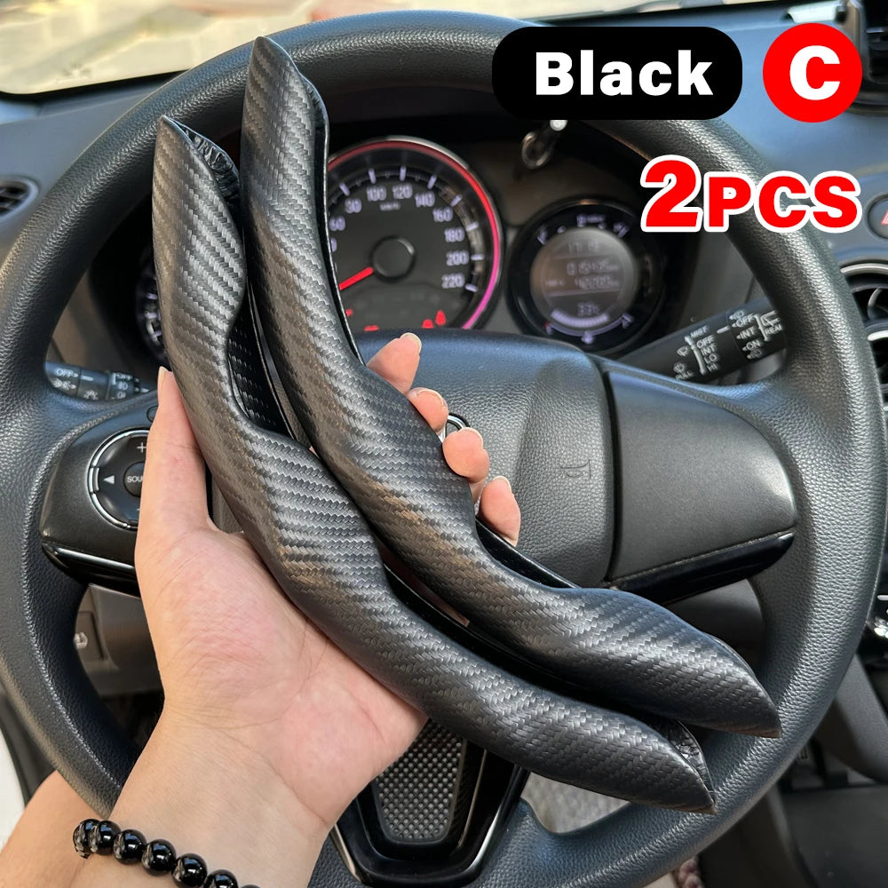 A hand holds a black carbon fiber steering wheel booster cover for a car.